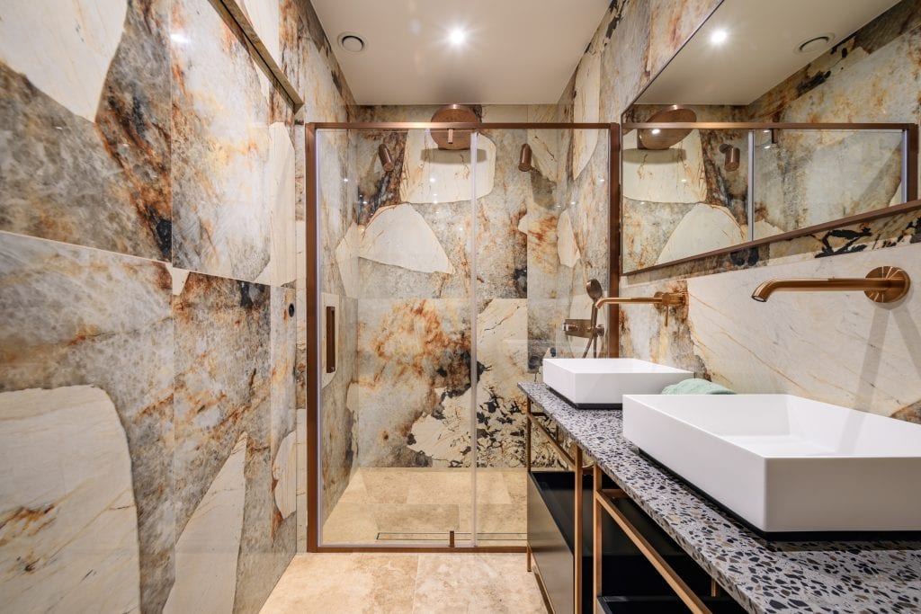 Luxury bathroom with stone wall tiles, walk-in shower, and double sinks.