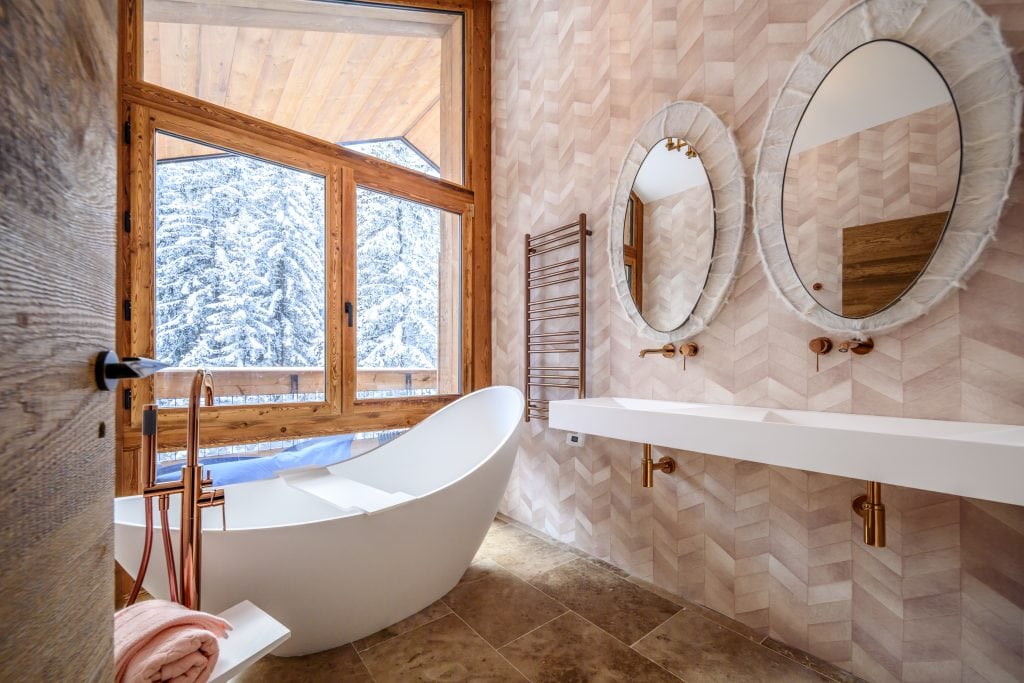 Bathroom with freestanding bathtub, large windows, and forest view.