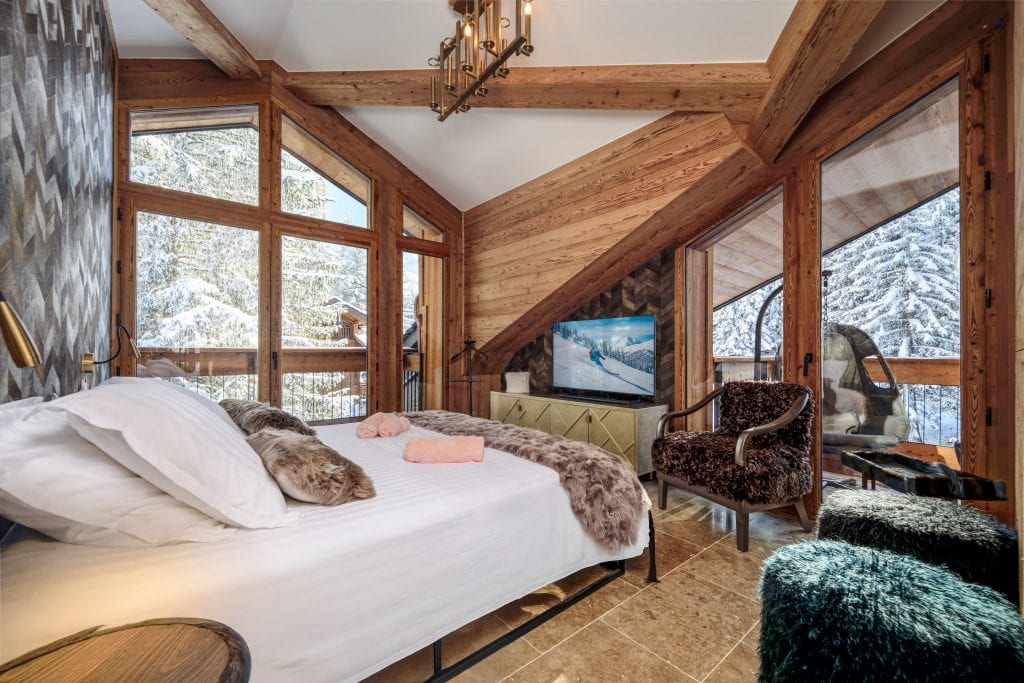 Bright alpine bedroom with large windows, forest view, and elegant decor.