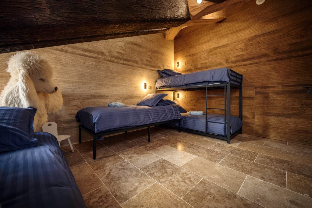 Kids bedroom with single beds, bunk beds, and warm wooden walls.