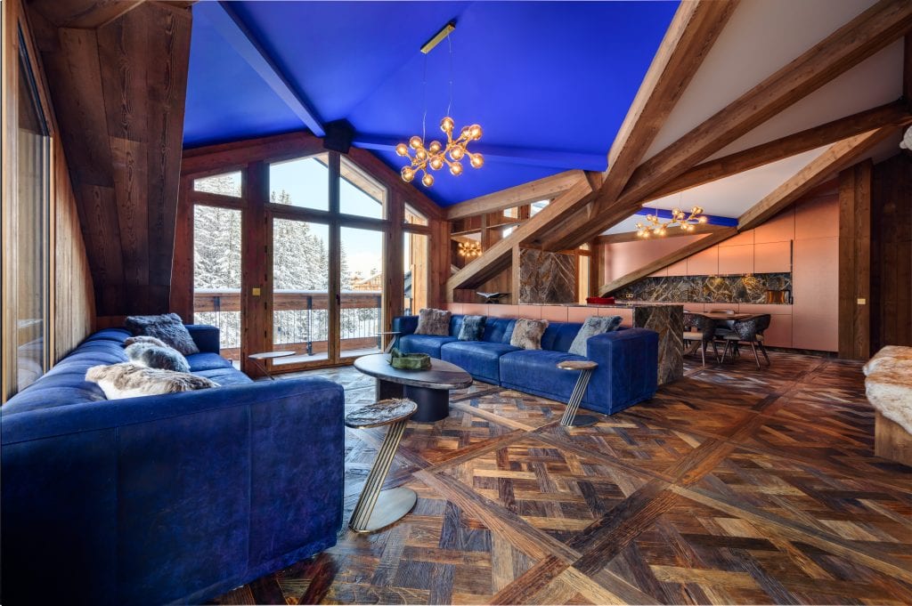 Spacious living room with blue sofas, open kitchen, and panoramic forest views.