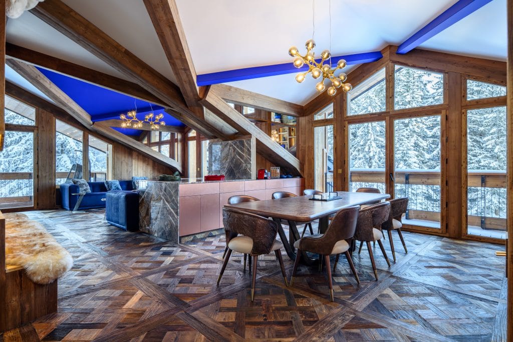 Dining room with wooden table, designer chairs, and large windows overlooking snowy trees.