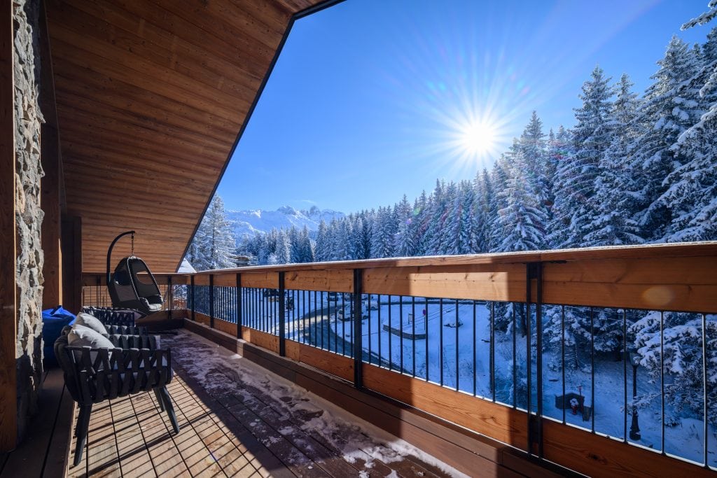 Balcony with lounge chairs facing a snowy forest and mountains at sunrise.